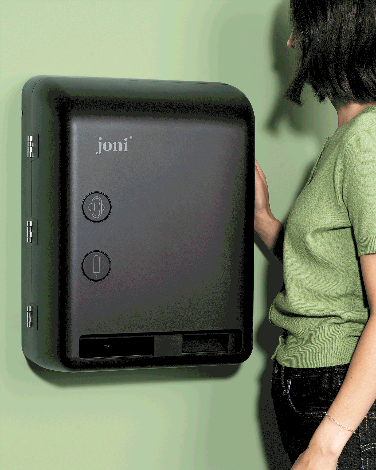 Person in green reaching for a wall-mounted joni period care dispenser