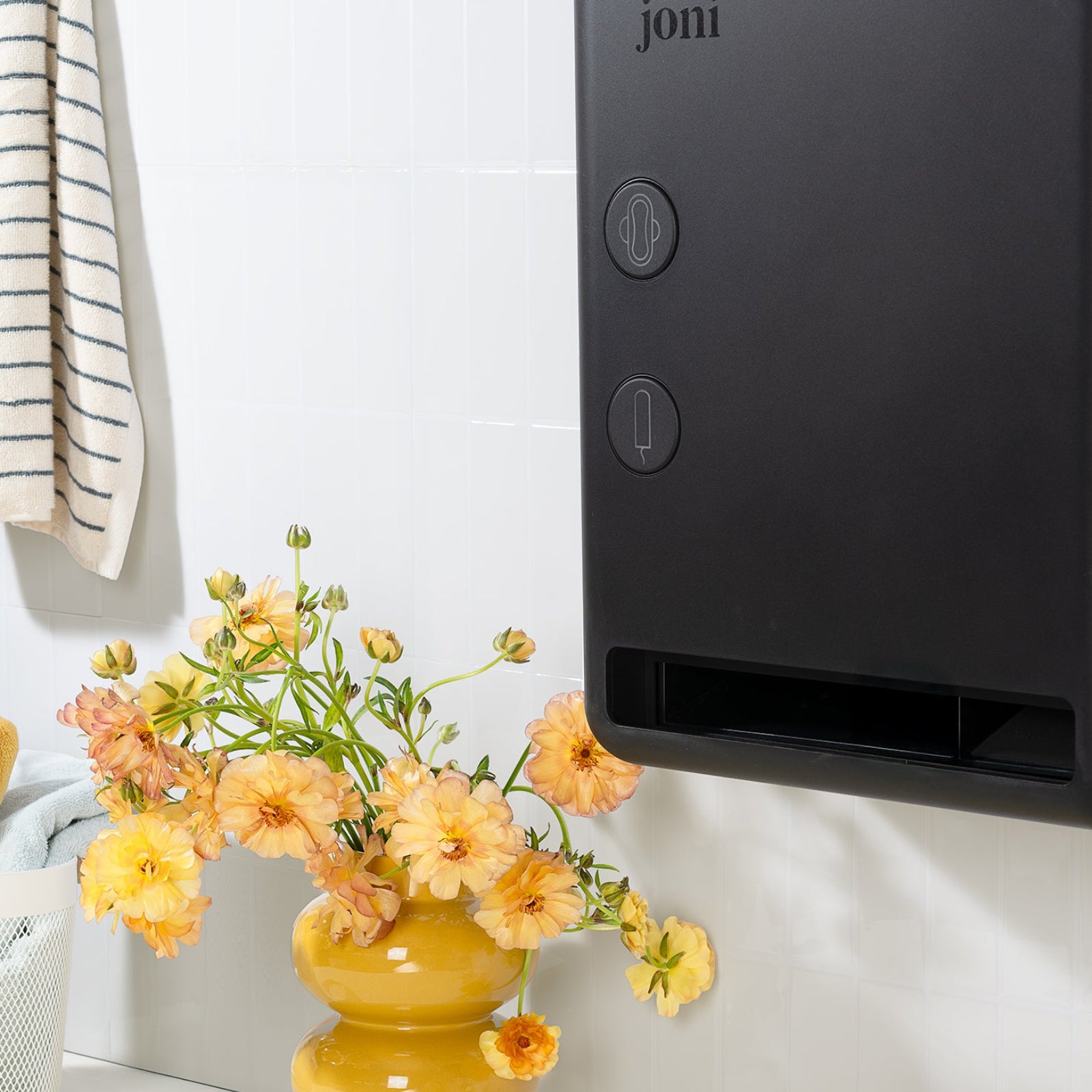 joni period care dispenser mounted in a bright washroom beside a vase of flowers