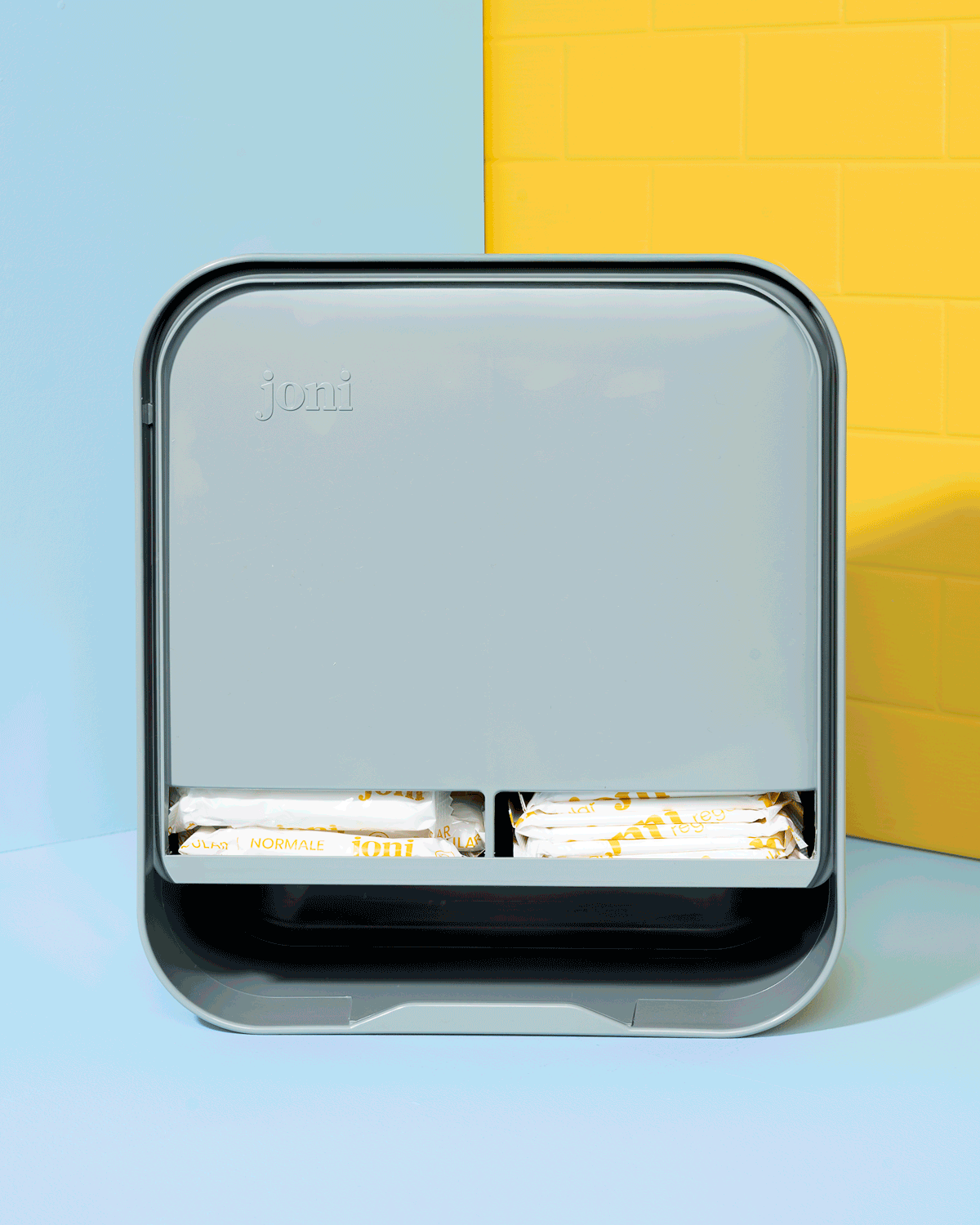 joni period care dispenser open on a blue and yellow tiled background