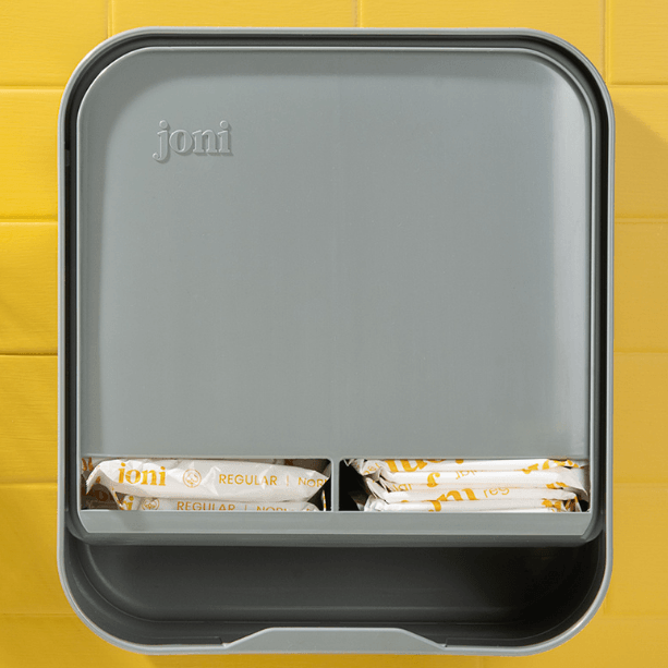 joni Model A open period care dispenser on a yellow brick wall