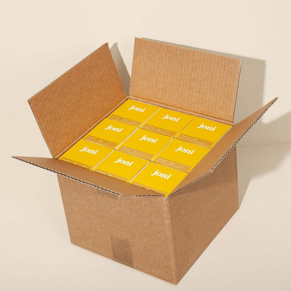 An open brown cardboard shipping box containing boxes of joni tampons for commercial 