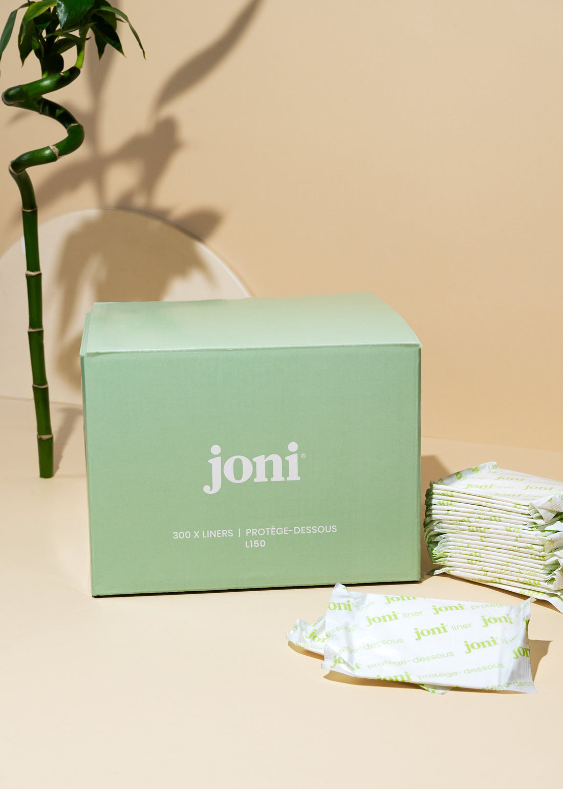 Bulk box of joni bamboo liners beside stacked liners and a bamboo stem